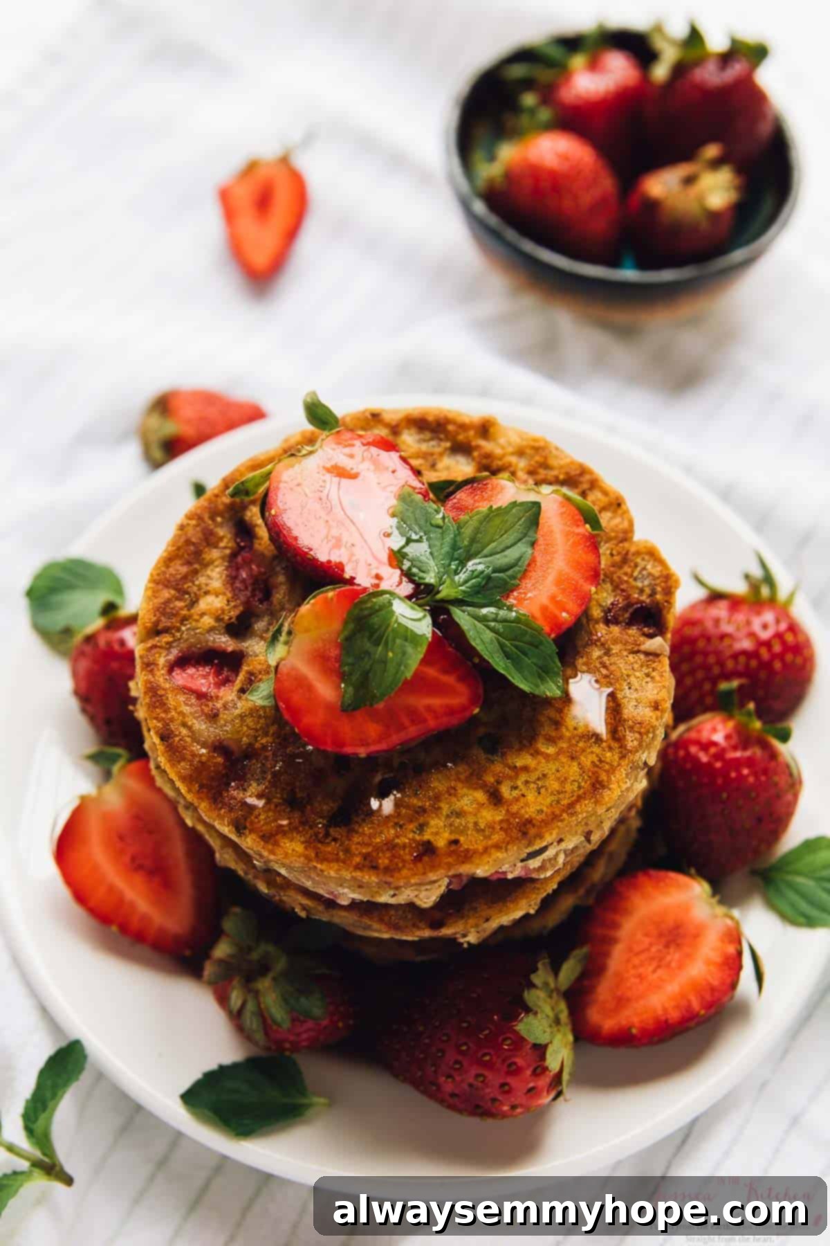 A stack of fluffy strawberry pancakes on a white plate, elegantly garnished with fresh whole berries and a cascade of maple syrup.