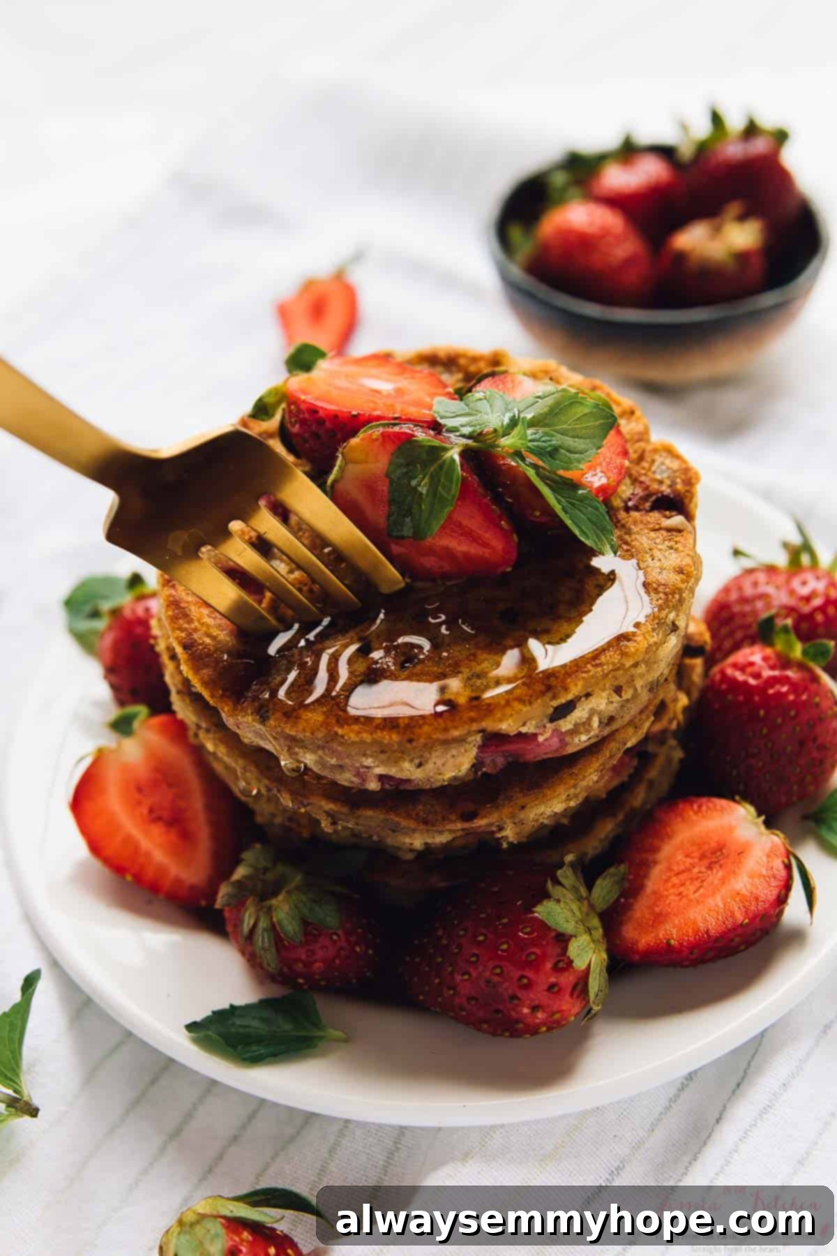 A fork taking a bite out of a stack of fluffy strawberry pancakes, topped with syrup and fresh berries, showcasing the tender interior.