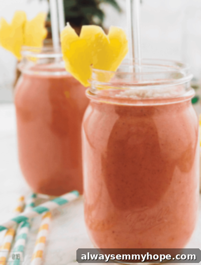 Seven Day Smoothie Reset Win A Prize 11 Two clear mason jars holding frothy, vibrant strawberry pineapple pina colada smoothies, garnished with fruit, ready to be enjoyed as a refreshing tropical drink.