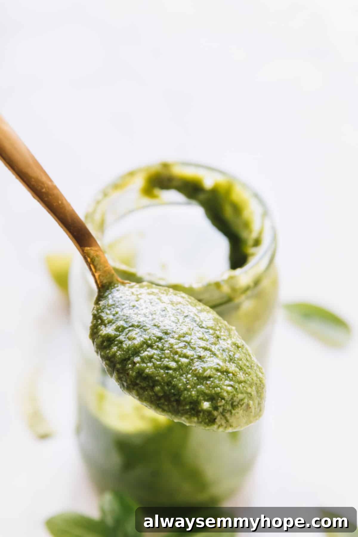 Spoonful of basil pesto held in front of a glass jar, highlighting its texture.