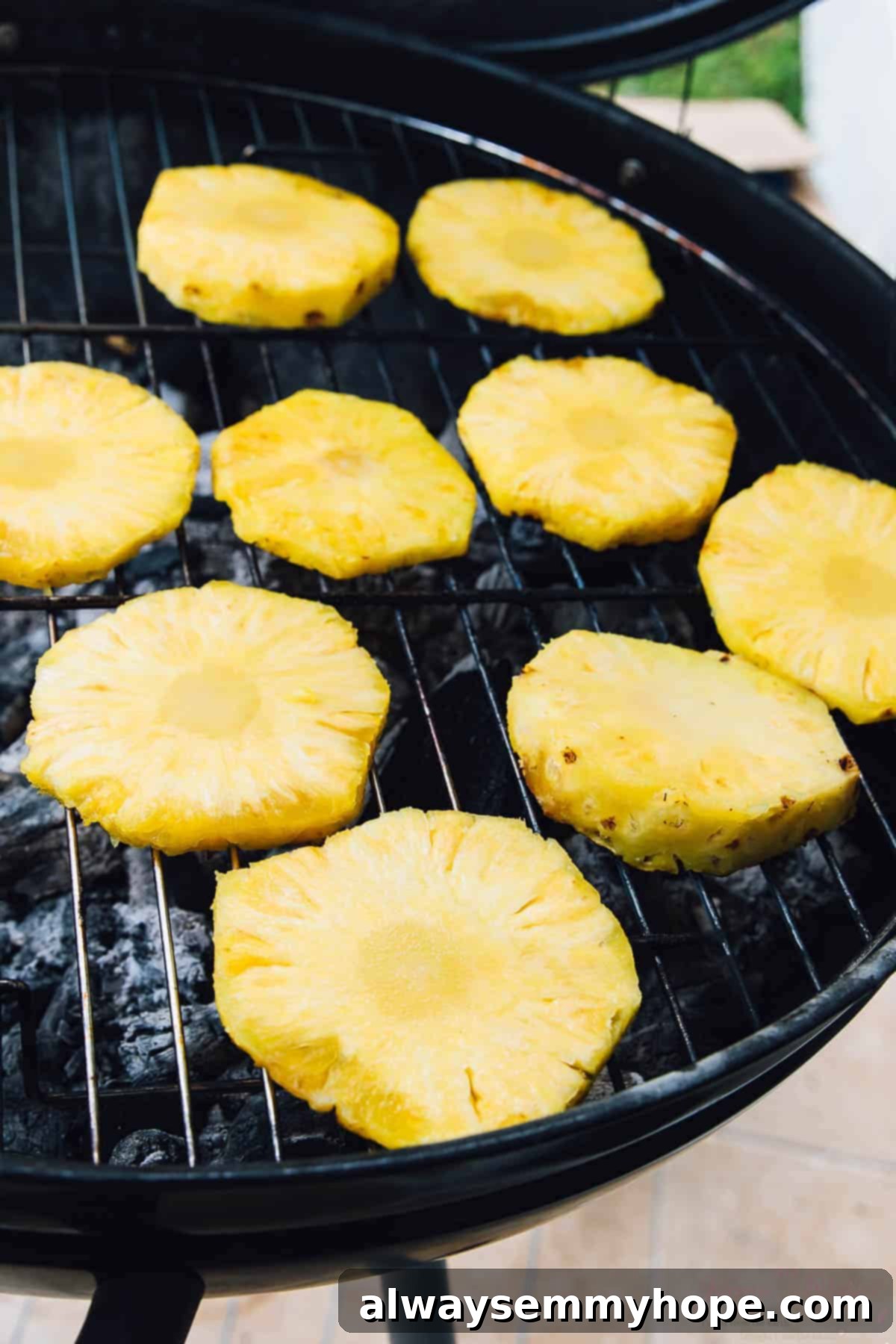 Thick slices of fresh pineapple sizzling on the grates of a hot BBQ grill, showing developing grill marks.