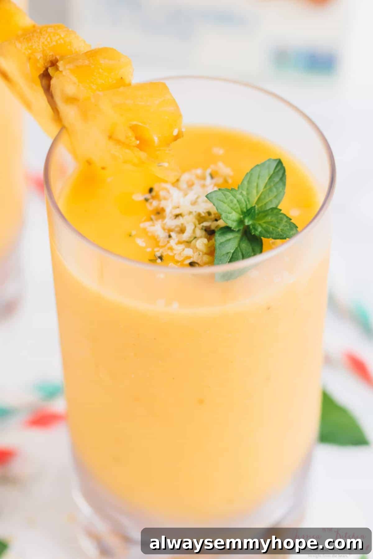 A refreshing pineapple peach smoothie served in a clear glass, garnished with fresh mint leaves.