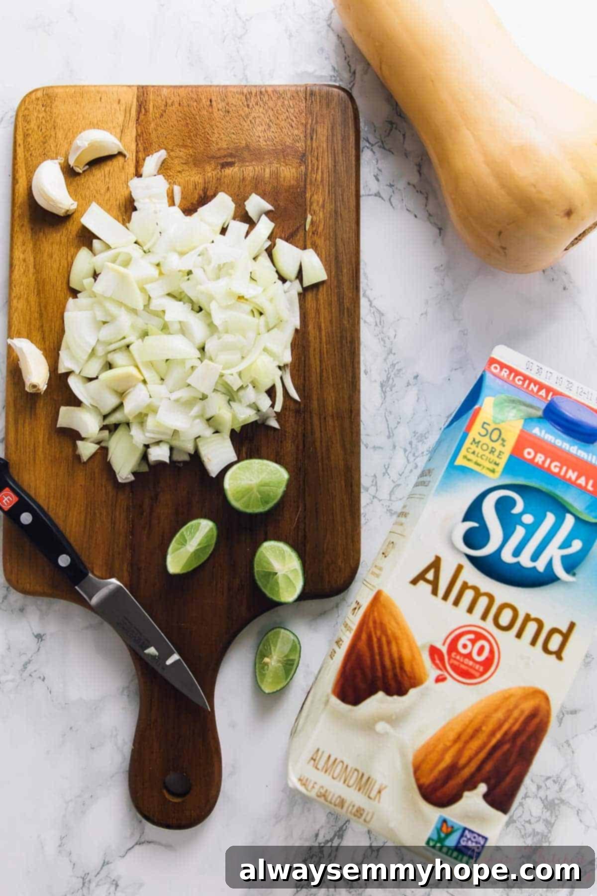Top down shot of diced onions, lime wedges, butternut squash and a carton of almond milk. 