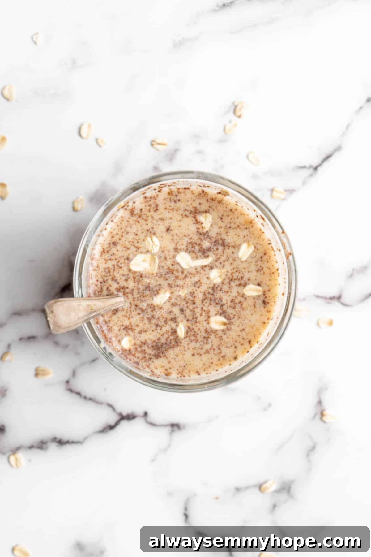 Overhead view of overnight oats in a glass jar with a spoon, showing the layered ingredients.