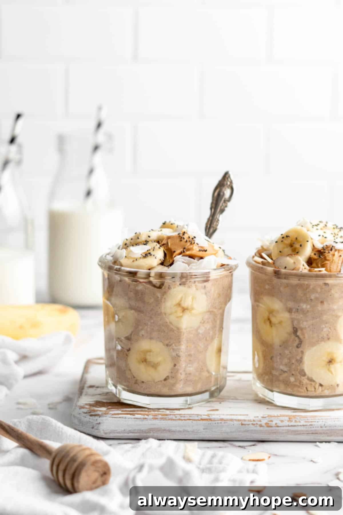 Two jars of overnight oats with banana slices, peanut butter drizzle, and a spoon in one.