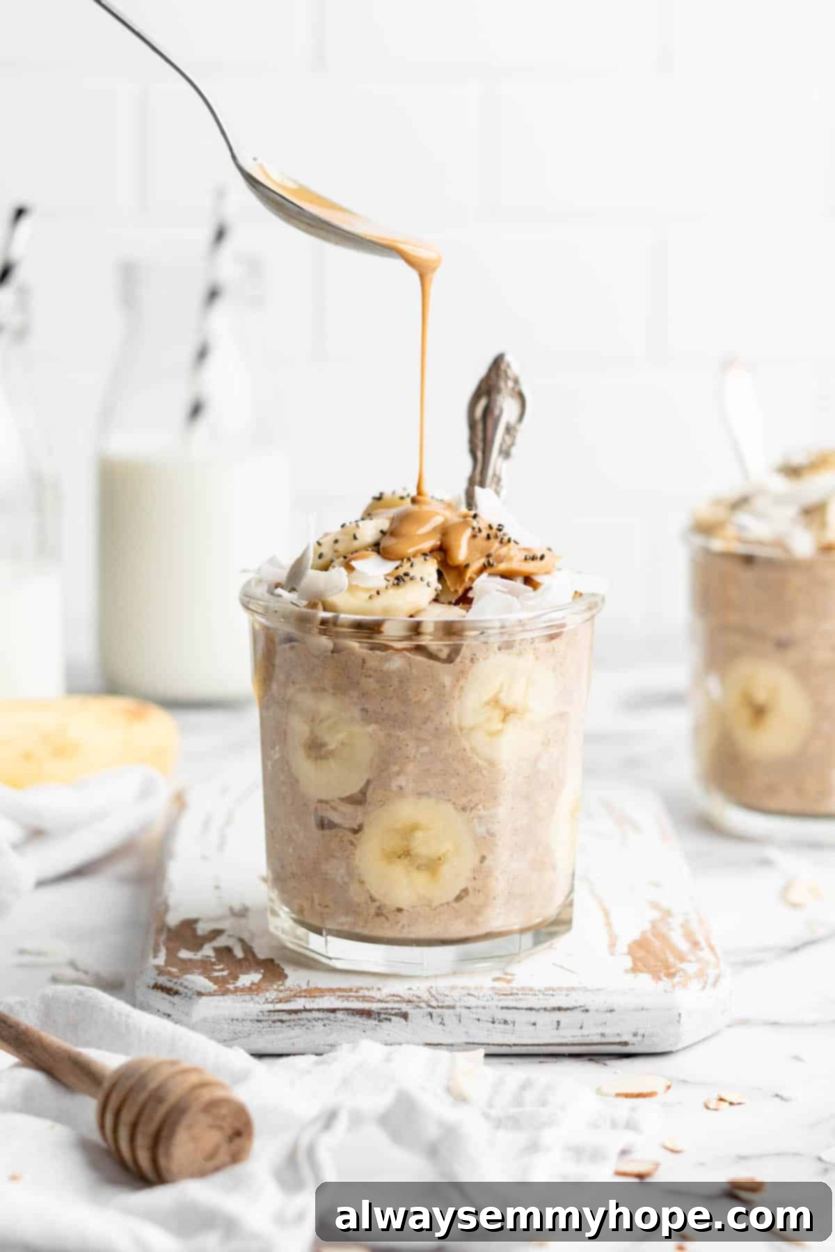 Spoon layering peanut butter over jar of overnight oats with banana slices.