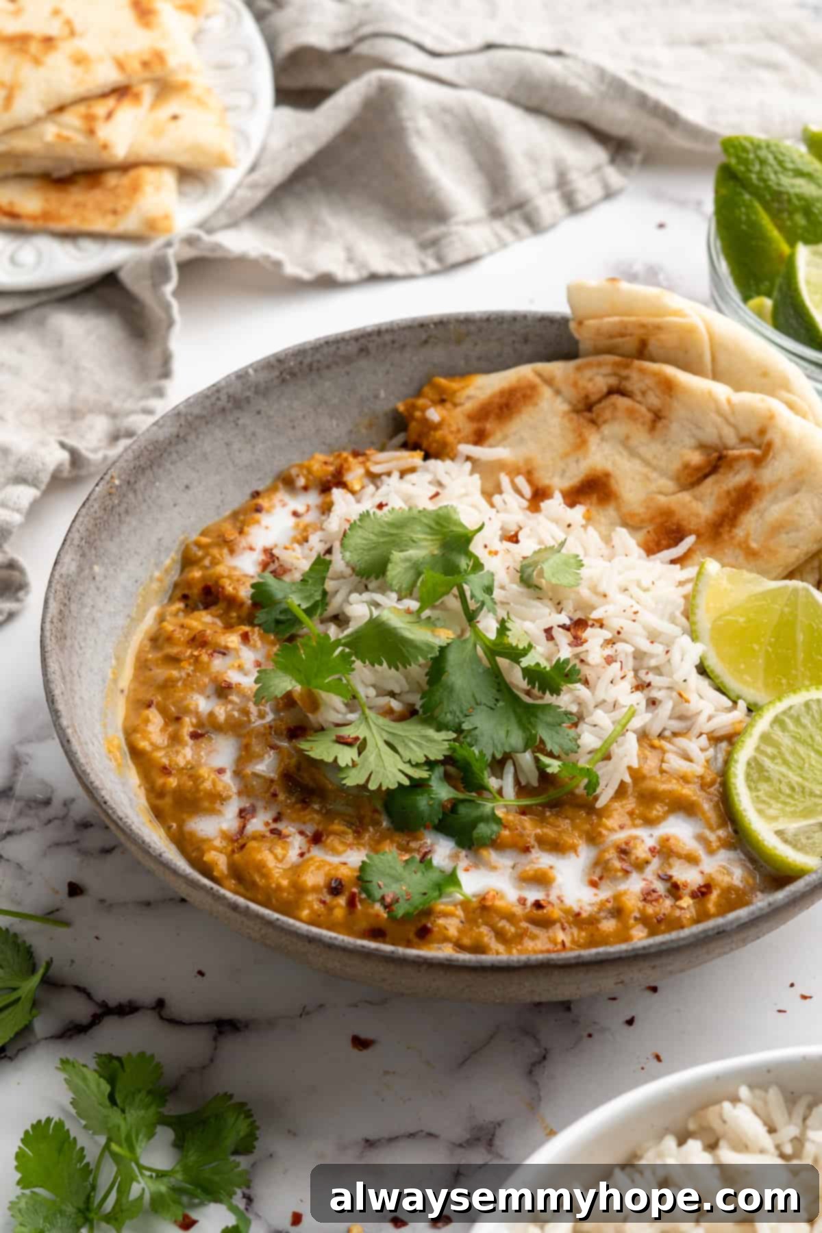 This red lentil curry is classic vegan comfort food! It’s a flavorful one-pot recipe that comes together in under an hour. A vibrant bowl of red lentil curry, garnished with fresh cilantro and served alongside fluffy rice and warm naan bread, with lime wedges for added zest.