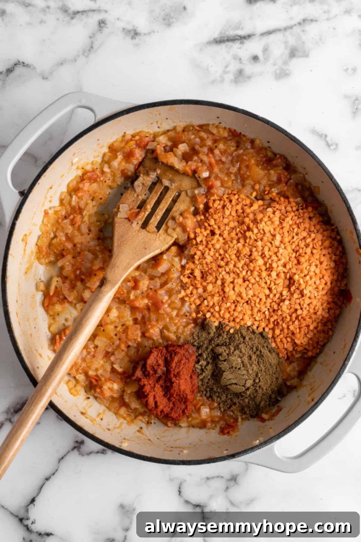 This red lentil curry is classic vegan comfort food! It’s a flavorful one-pot recipe that comes together in under an hour. Overhead view of dry red lentils and a medley of colorful spices being added to the cooked onion and tomato base in a pot, ready to be stirred.