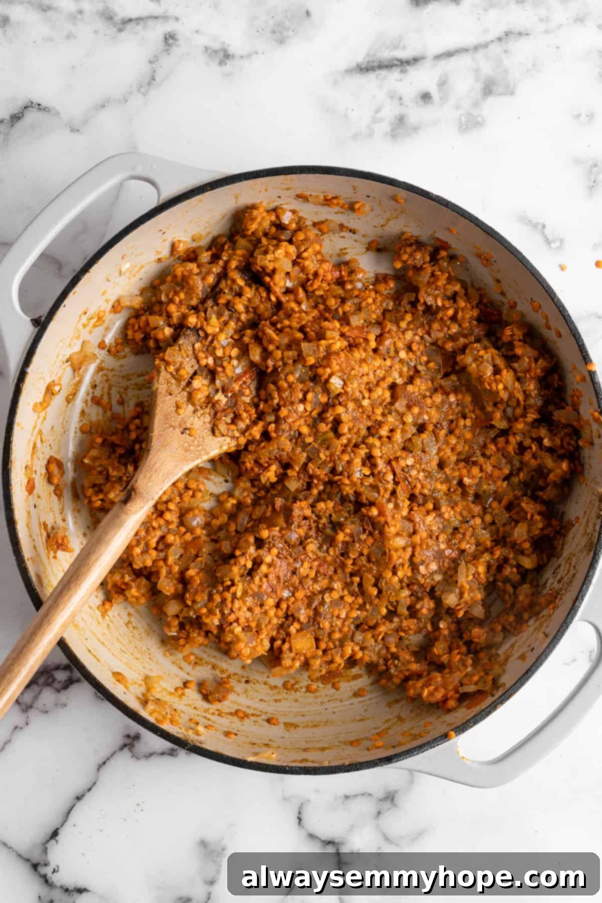 This red lentil curry is classic vegan comfort food! It’s a flavorful one-pot recipe that comes together in under an hour. Overhead view of the red lentil curry in a pot after the lentils and spices have been thoroughly stirred into the aromatic base, creating a rich mixture.