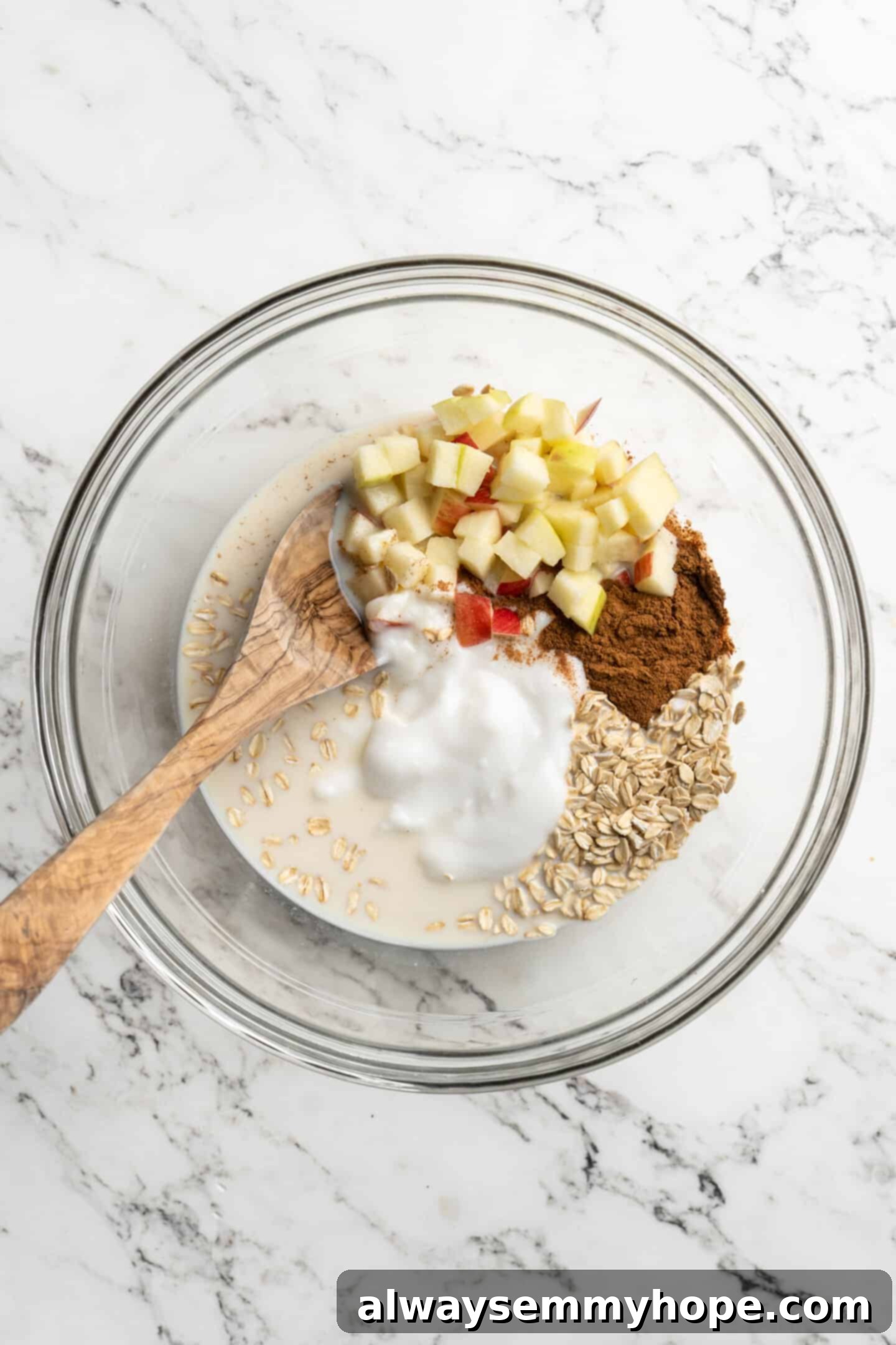 No-Bake Apple Pie Oats 2 Bowl of unmixed ingredients for overnight oats with a wooden spoon, showcasing oats, apples, and spices.