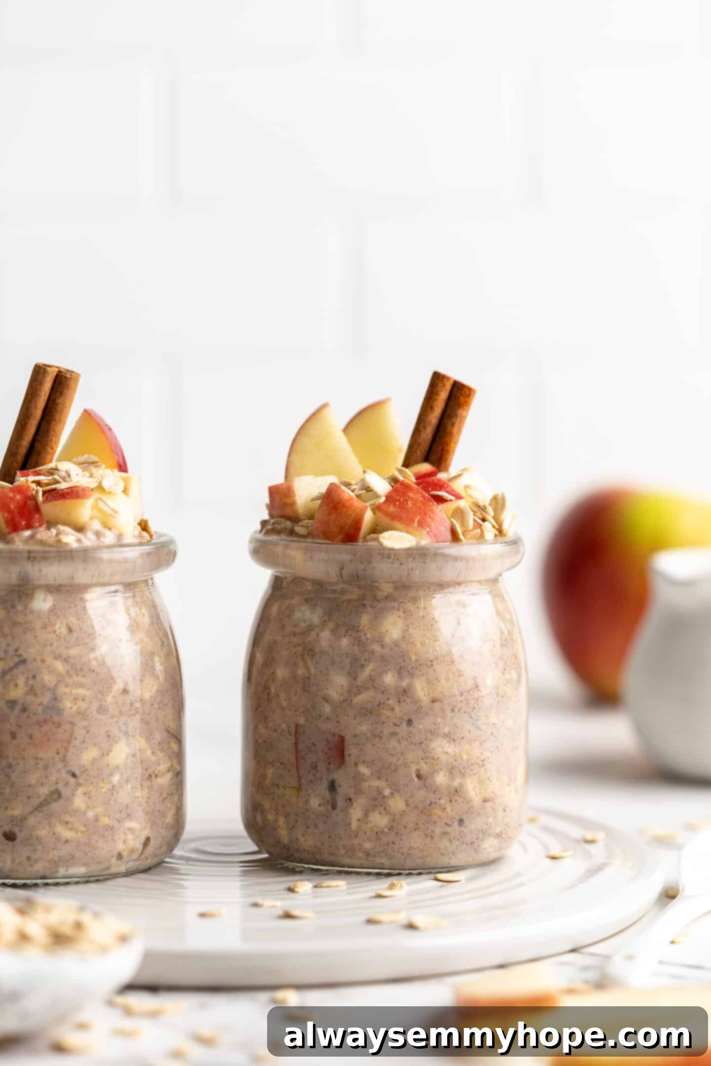 Apple pie overnight oats are packed with crisp apples, warm cinnamon, rich almond milk, and decadent maple syrup, and are an easy breakfast. Two side-by-side jars of apple pie overnight oats, garnished with cinnamon sticks, oats, and fresh apple slices.