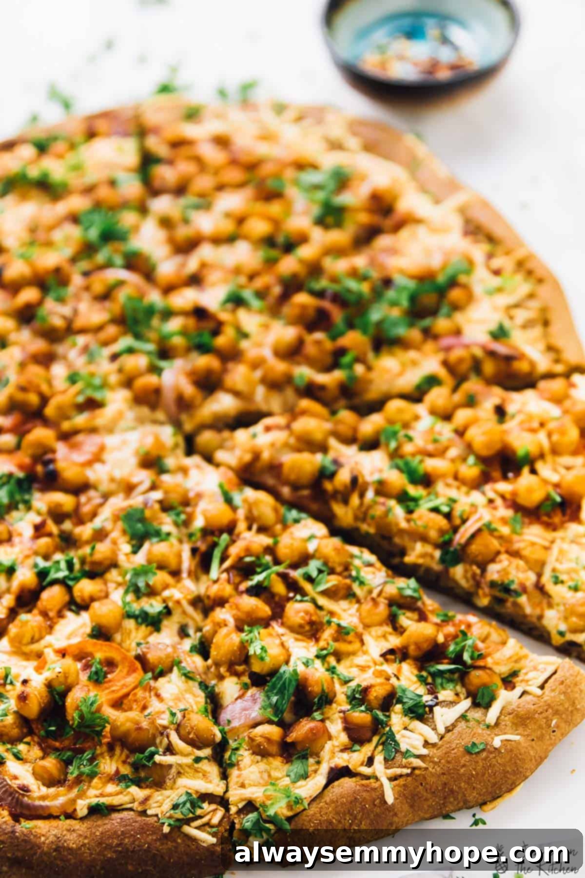 Spicy BBQ chickpea pizza: A delicious vegan alternative to BBQ chicken pizza, packed with flavor and ready in a flash. A perfectly baked slice of spicy BBQ chickpea pizza on a parchment-lined countertop, showcasing crispy chickpeas, melted vegan cheese, and fresh toppings.
