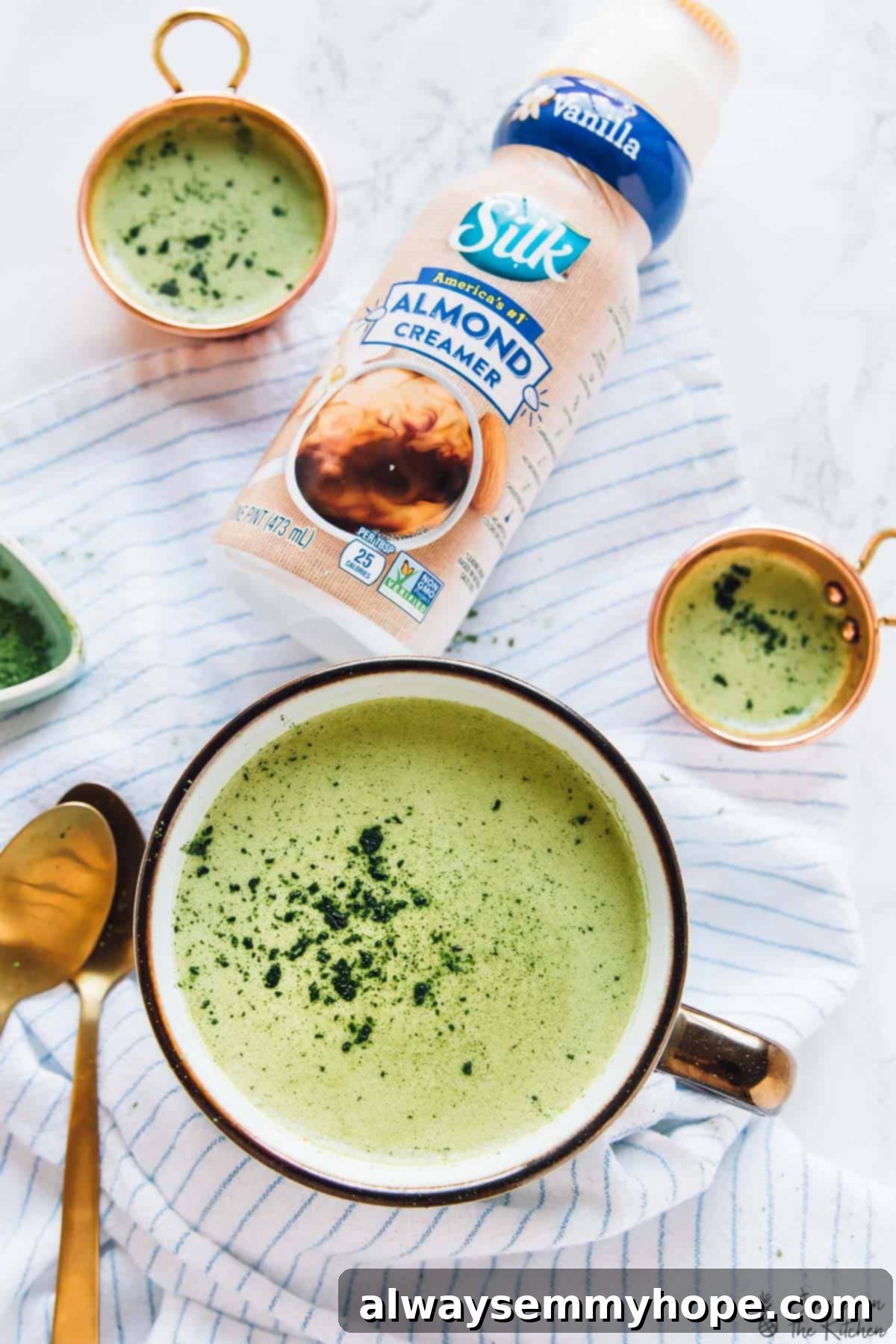 Creamy Pumpkin Matcha Latte A high-angle shot of a frothy Pumpkin Spice Matcha Latte in a white mug, positioned next to a clear glass bottle of almond creamer.