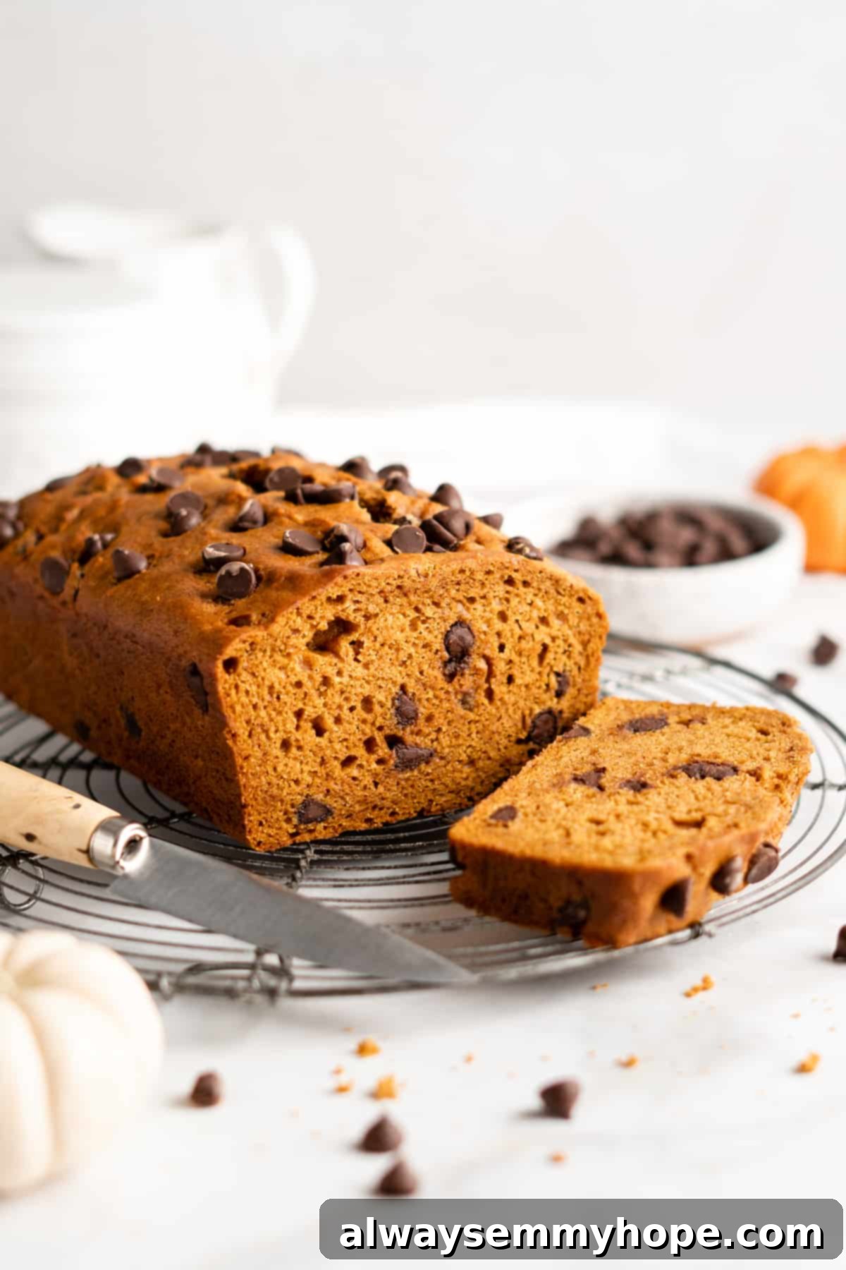 Freshly baked loaf of vegan chocolate chip pumpkin bread on a cooling rack with a knife, one slice already cut and revealing the moist interior and chocolate chips.
