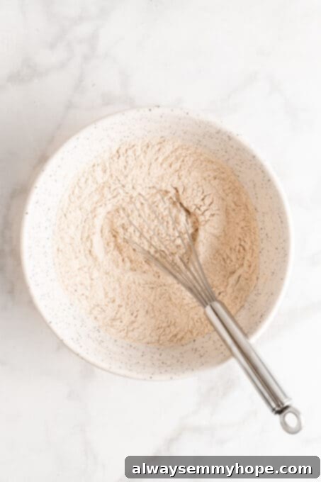Overhead view of dry ingredients (flour, baking powder, baking soda, salt, cinnamon, pumpkin pie spice) in a mixing bowl, ready to be whisked.