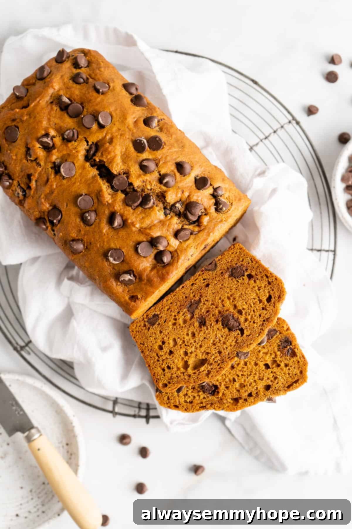 Two slices of vegan chocolate chip pumpkin bread placed next to a whole loaf on a cooling rack, showcasing the moist interior and melted chocolate chips.
