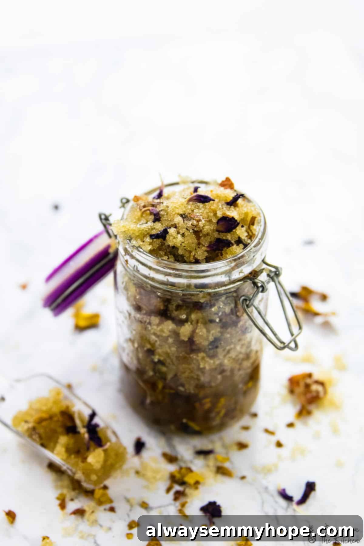Close-up of the coconut rose sugar scrub in a clear glass jar, showing the granular texture and pink flecks.