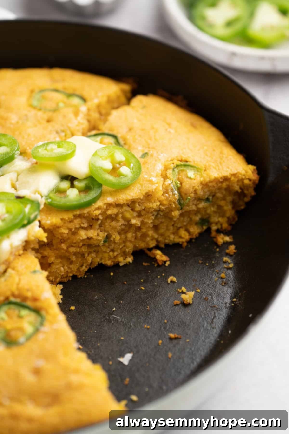 A whole vegan pumpkin cornbread baked in a cast iron skillet, viewed from an angle, showcasing its golden-brown top.