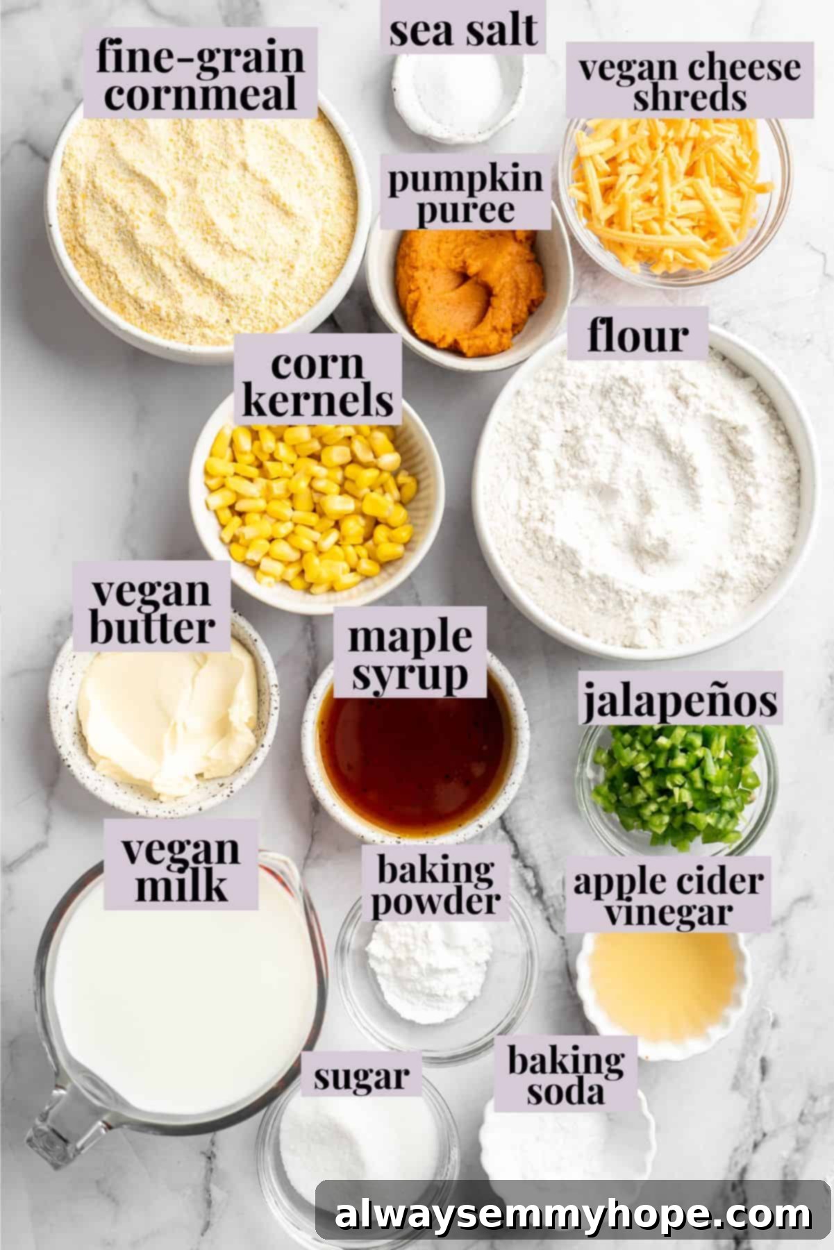 Overhead view of all the fresh ingredients for vegan pumpkin cornbread laid out on a table, including cornmeal, flour, pumpkin puree, jalapeños, and vegan cheese, each clearly labeled.