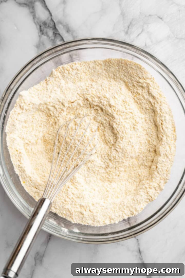 A mixing bowl filled with dry ingredients for vegan pumpkin cornbread, including cornmeal and flour, being whisked together thoroughly.