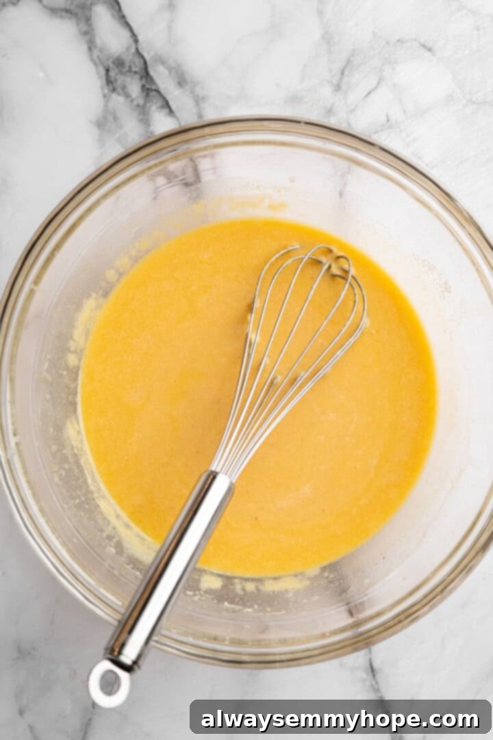 A bowl of wet ingredients for vegan pumpkin cornbread, including pumpkin puree, vegan buttermilk, melted vegan butter, sugar, and maple syrup, stirred until smooth.