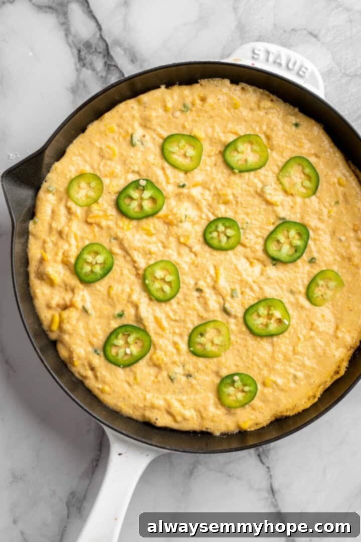 Vegan pumpkin cornbread batter poured into a hot cast iron skillet, with a few fresh jalapeño slices arranged on top before baking.