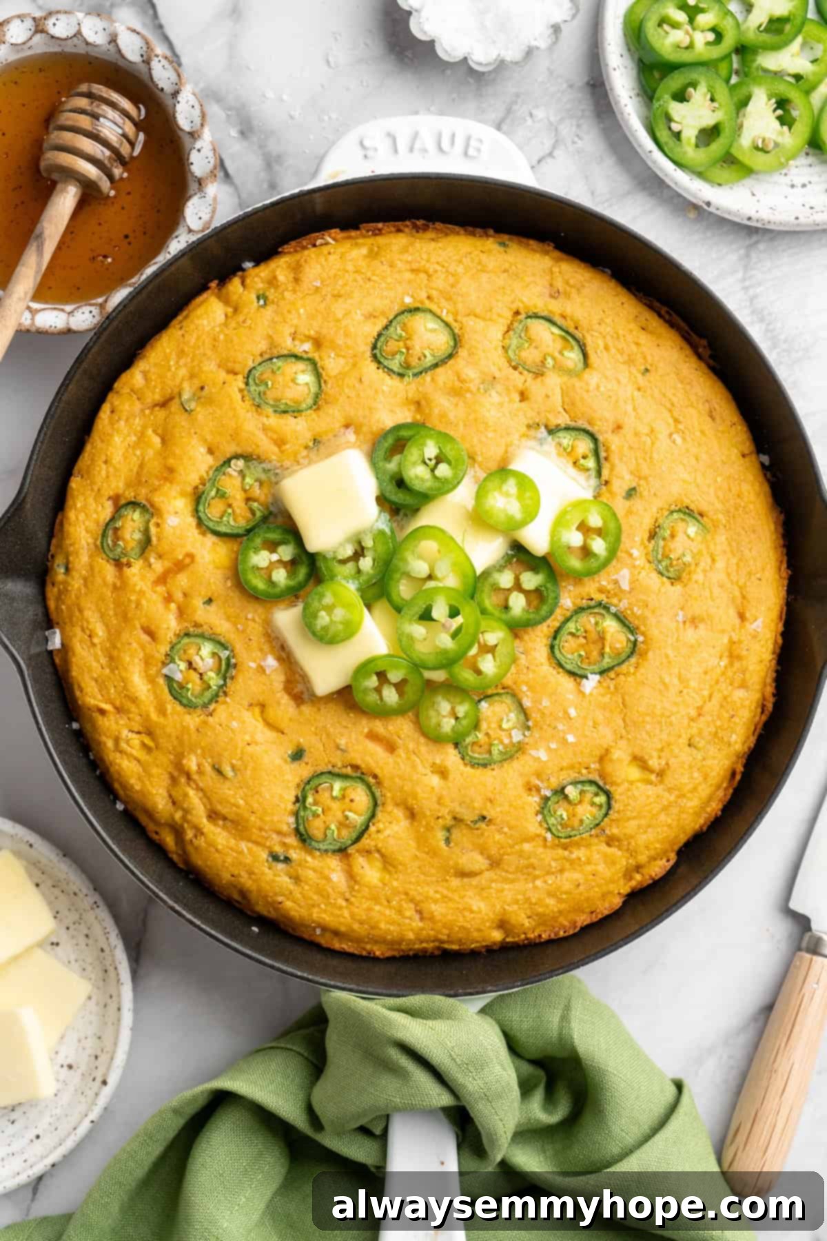 Freshly baked vegan pumpkin cornbread in a cast iron skillet, garnished with a dollop of vegan butter and fresh jalapeño slices.