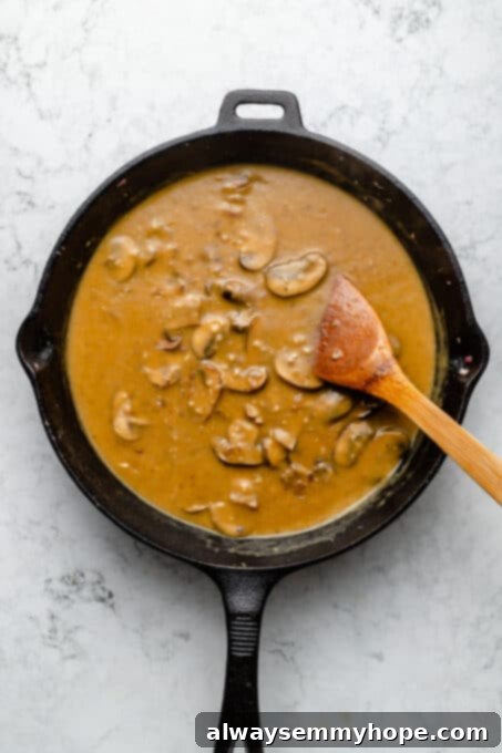 Overhead view of creamy mushroom sauce in cast iron skillet with wooden spoon