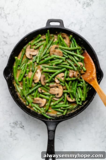 Overhead view of green beans and mushrooms in skillet with wooden spoon