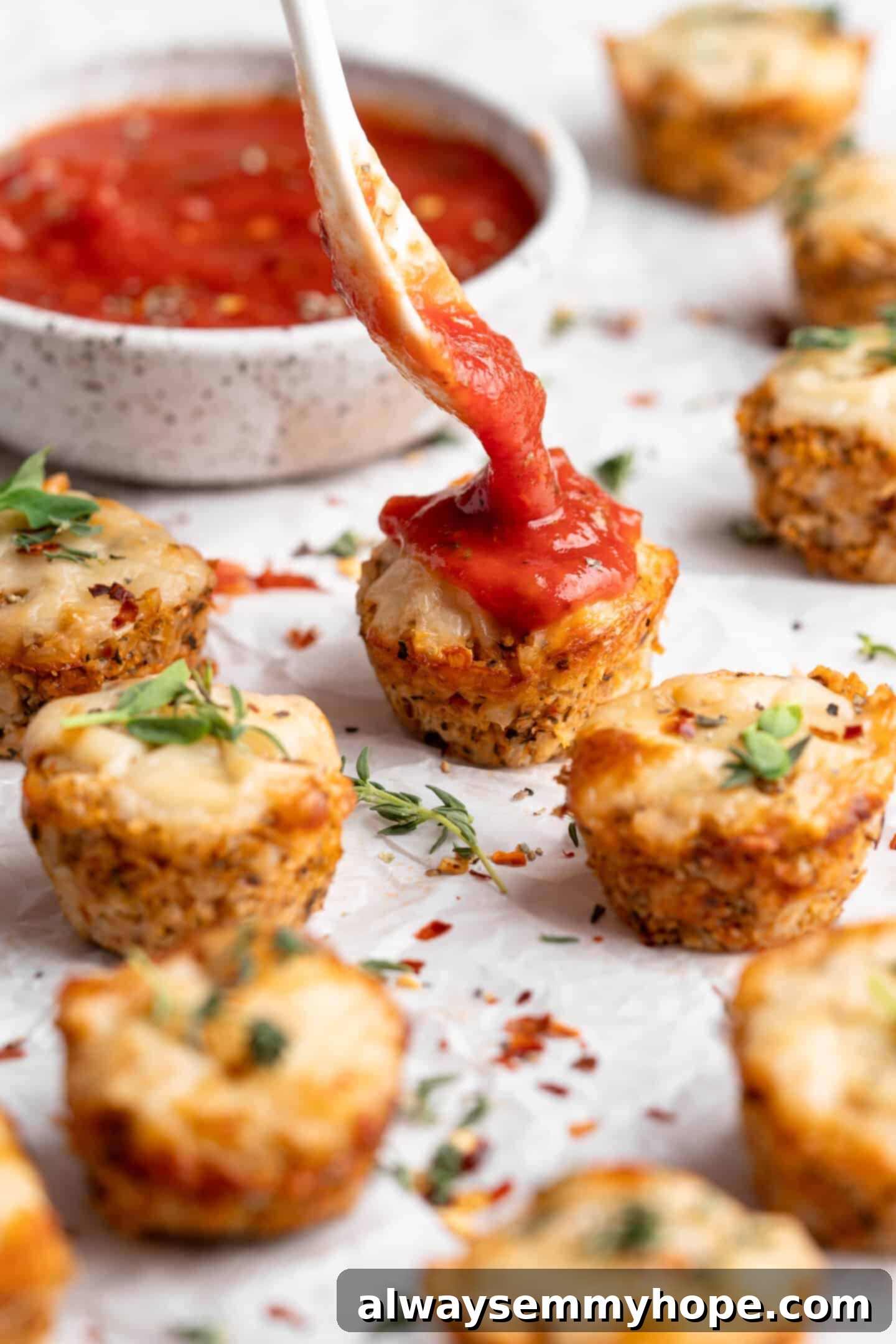 Freshly baked vegan cauliflower pizza bite being spooned with vibrant marinara sauce, showcasing its cheesy texture and inviting aroma.