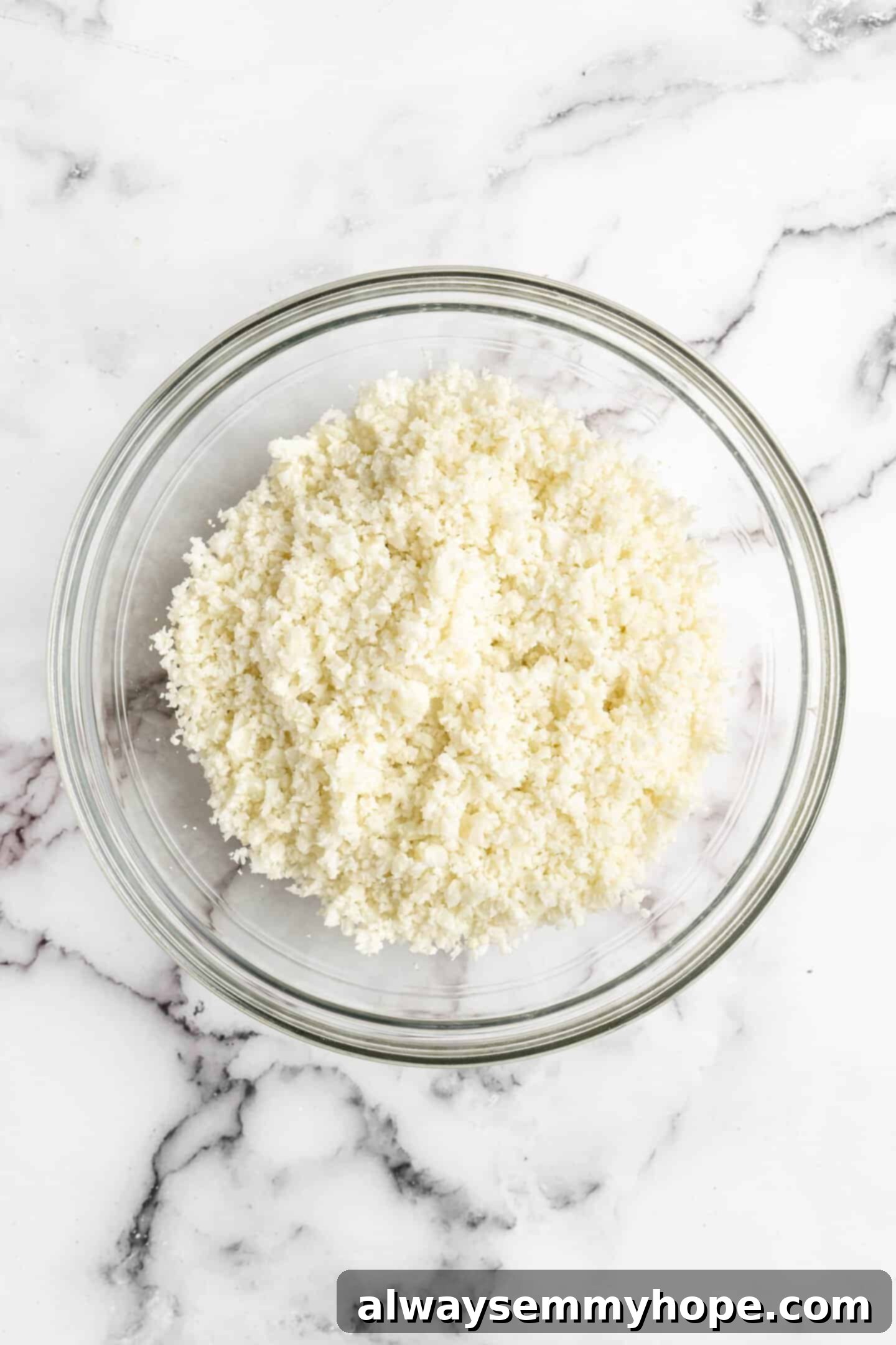 Finely riced fresh cauliflower ready in a glass bowl, illustrating the essential first step for healthy pizza bites.
