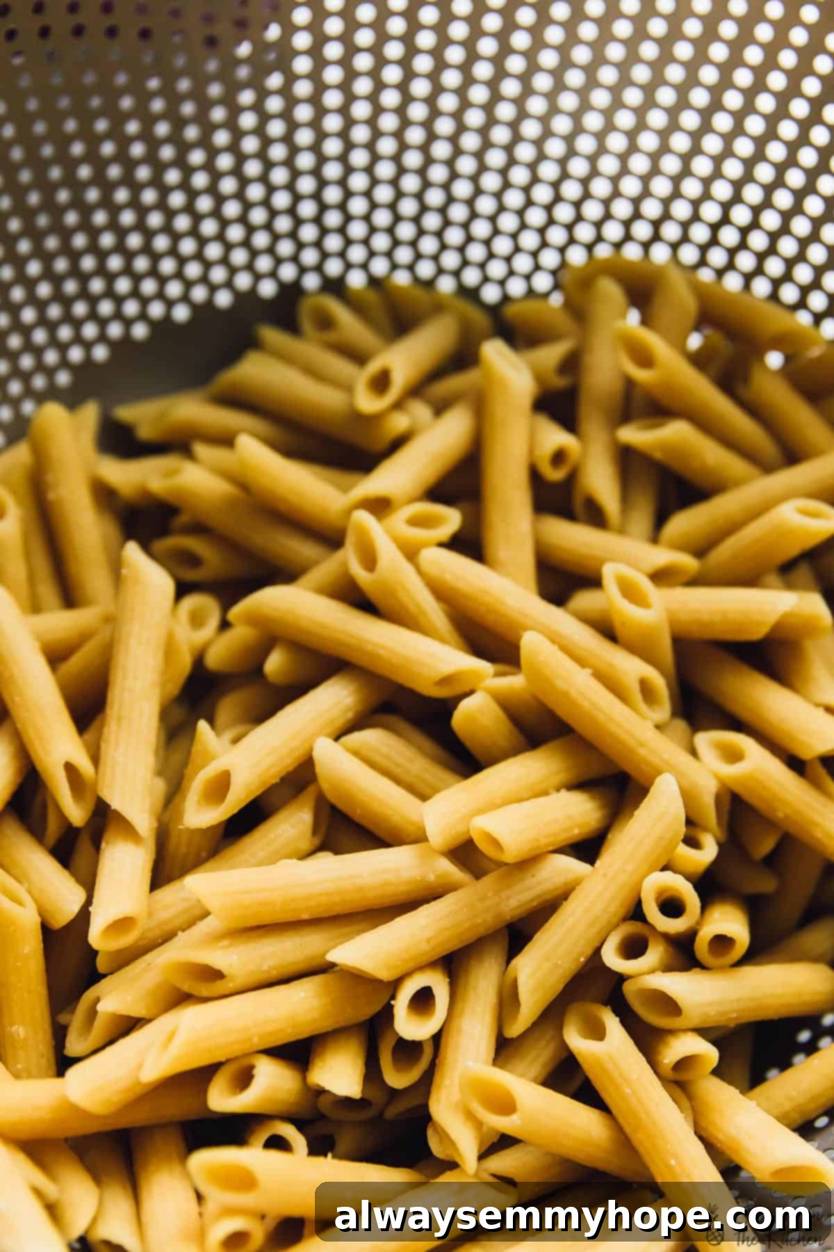 Overhead view of cooked pasta glistening in a colander, ready to be incorporated into the bake.