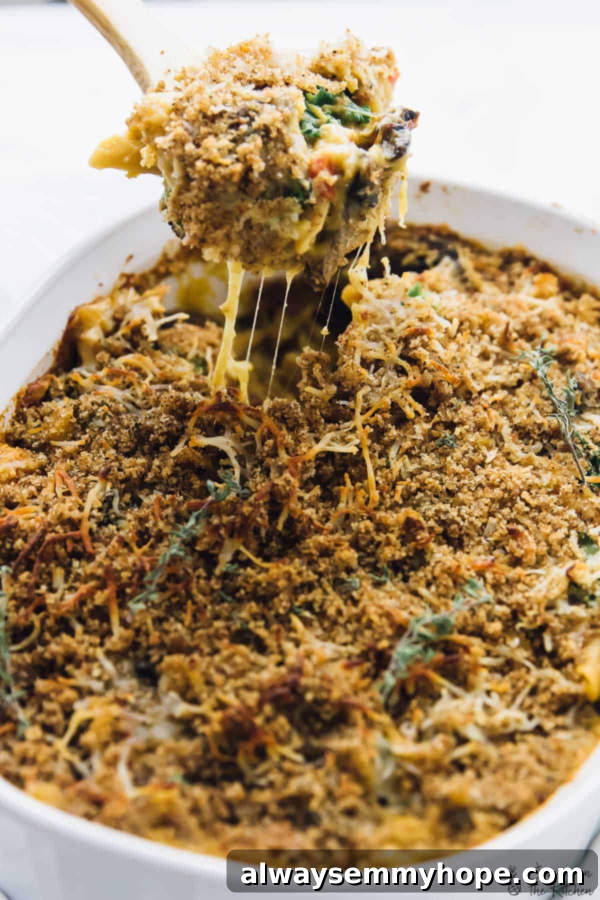 A spoon delicately scooping up a portion of creamy butternut squash pasta bake from a pristine white baking dish, showcasing its rich texture.