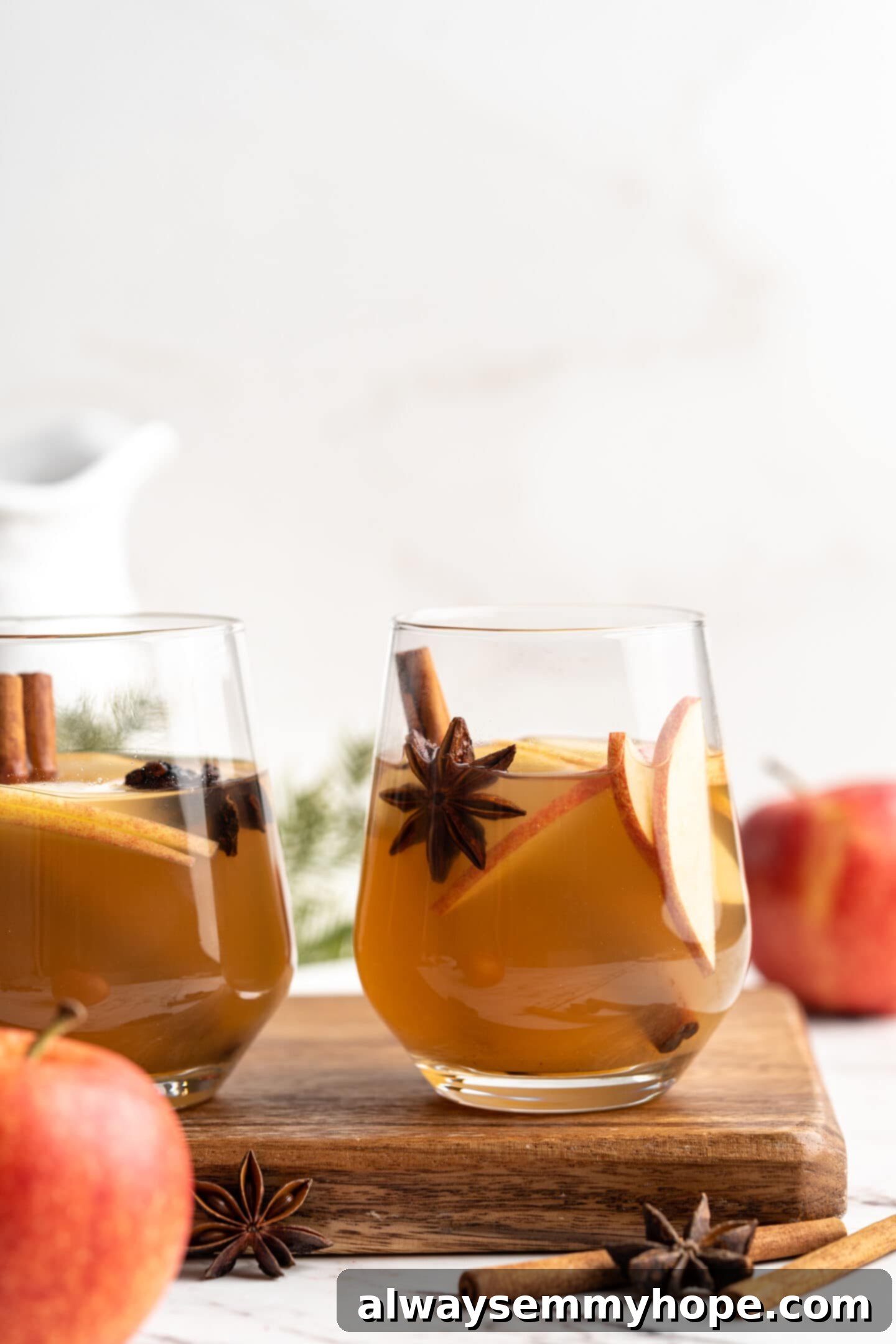 Two steaming glasses of hot spiced apple cider, garnished with cinnamon sticks and orange slices, set on a rustic wooden board, creating a cozy and inviting scene.