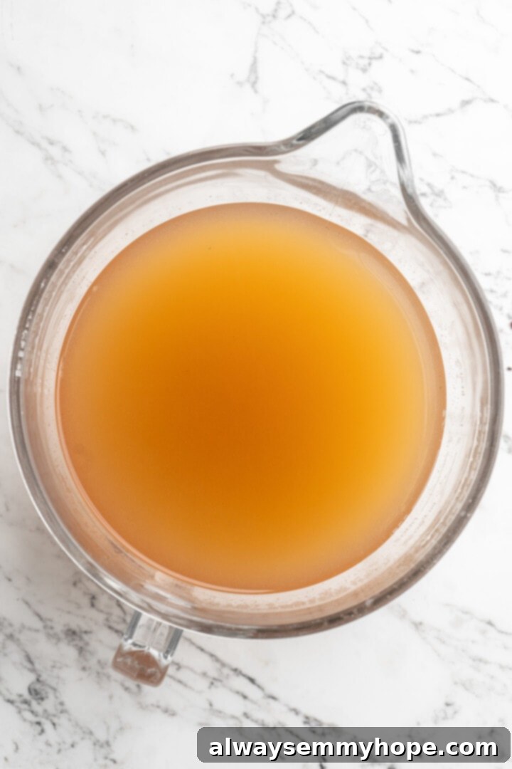 Overhead view of clear, rich amber-colored hot spiced apple cider in a glass bowl after straining, ready to be served or reheated.