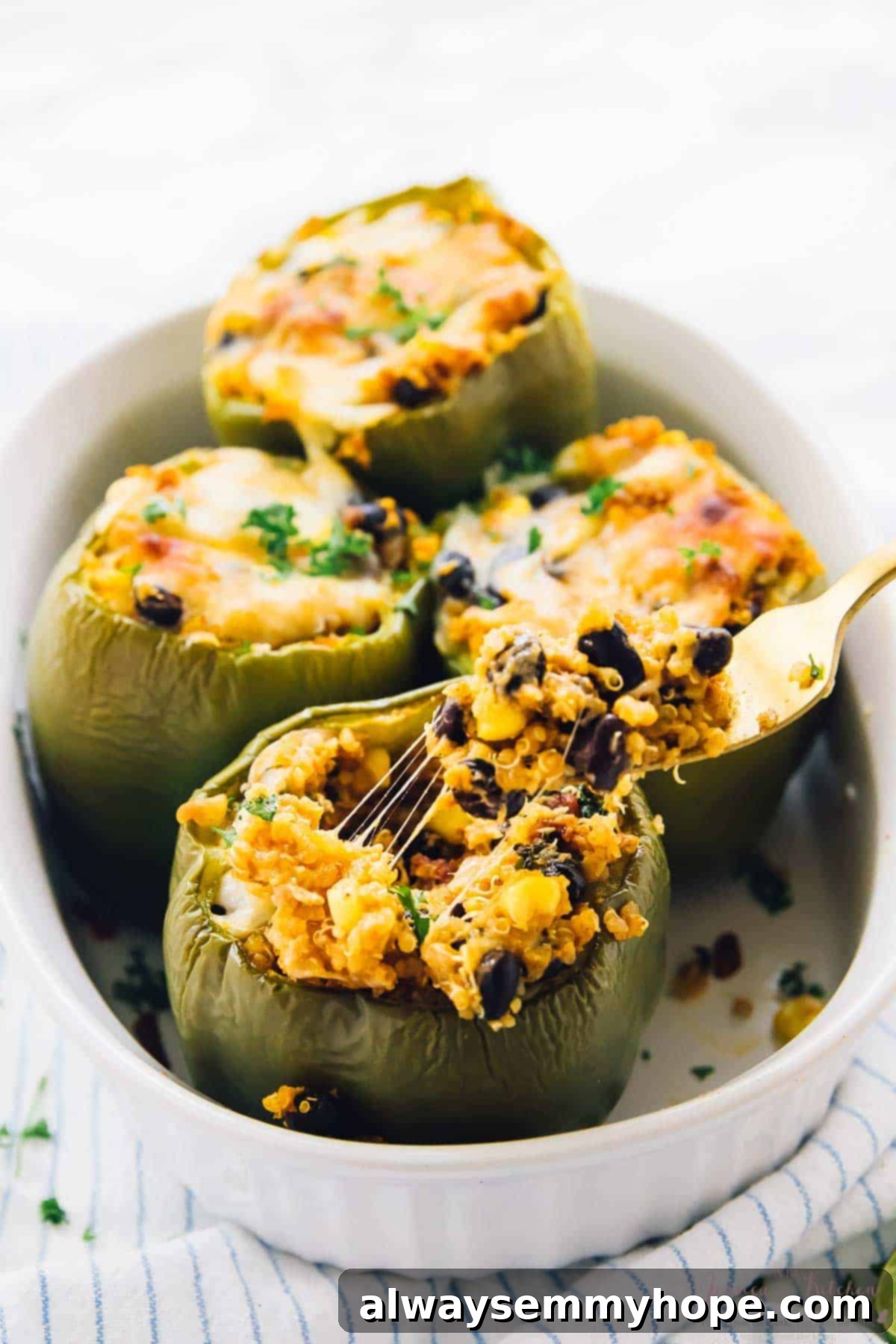 Four quinoa stuffed peppers in a white baking dish.