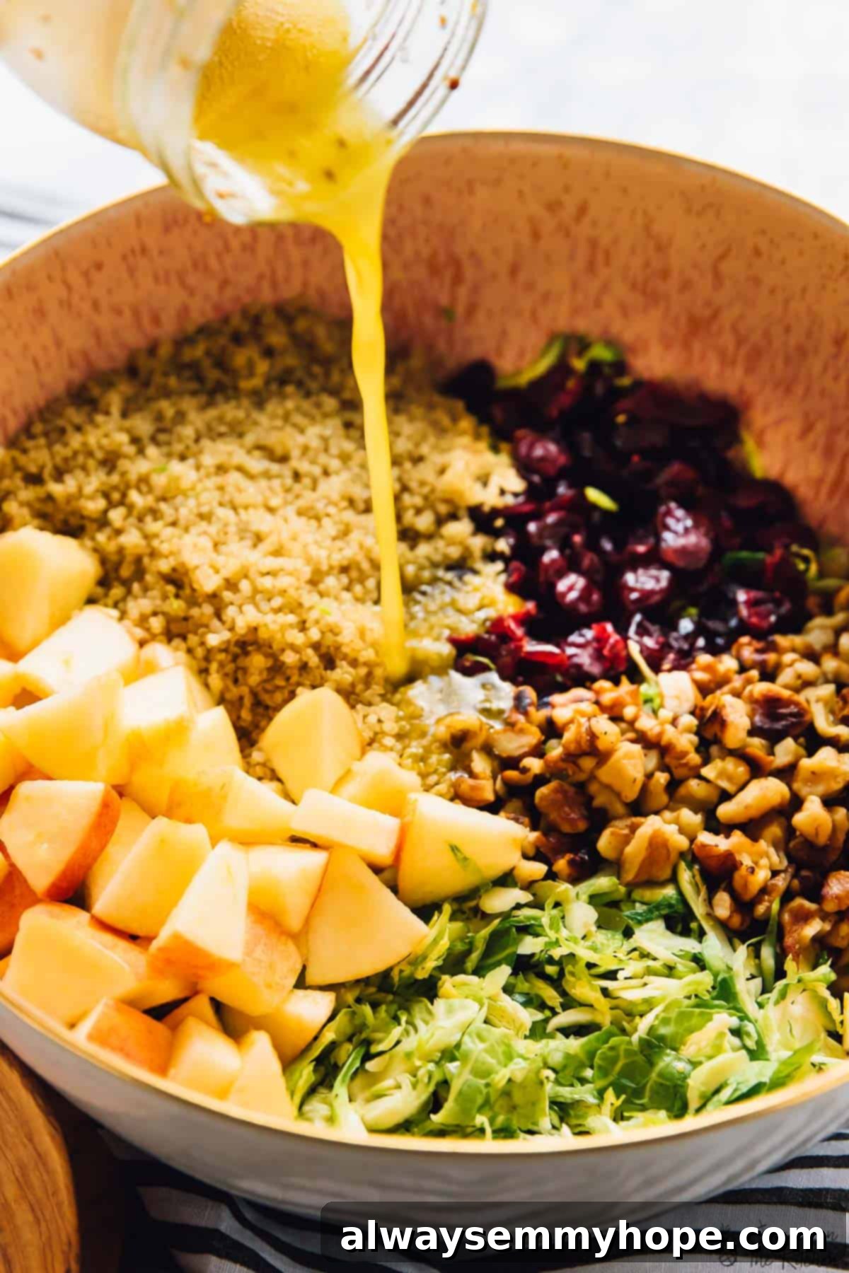 Pouring vinaigrette onto shaved brussels sprouts, quinoa and apple salad.