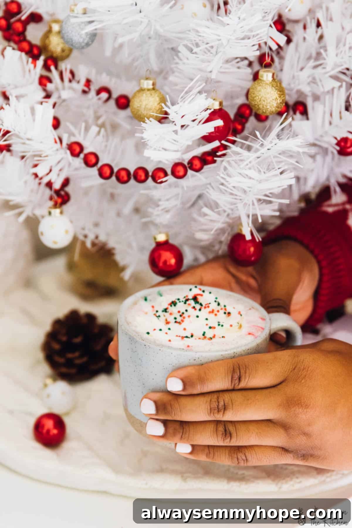 5 Ways to Find Holiday Calm, No Cooking Required 4 Hands holding a cup of hot chocolate, gently placed on a cozy white blanket with a festive backdrop.