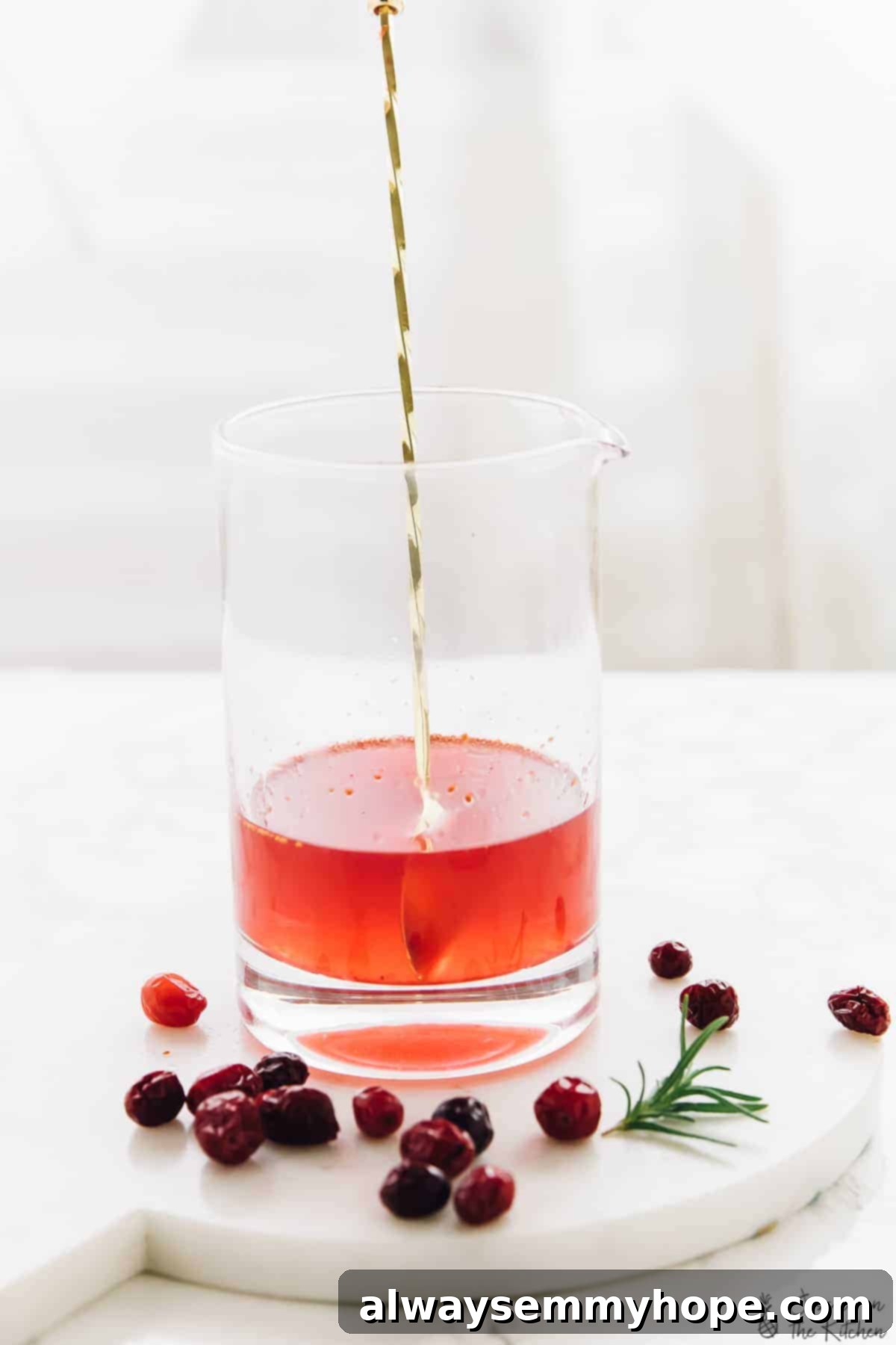 A gold spoon stirring a cranberry gin cocktail in a glass. 