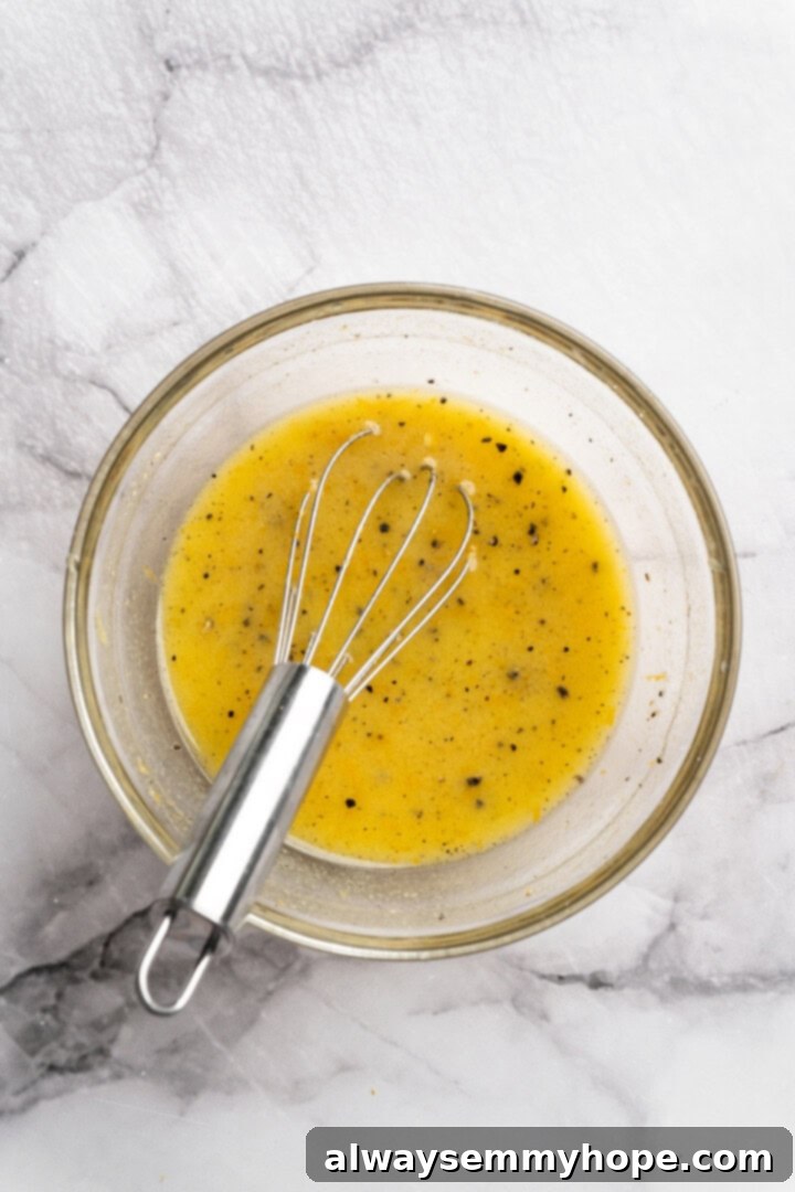 Orange vinaigrette in a glass bowl, being whisked gently with a small whisk.