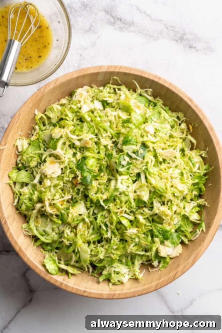 Shaved Brussels sprouts in a large serving bowl next to a small bowl of sweet orange vinaigrette.