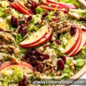 Shaved Brussels sprout salad with apples, walnuts, and cranberries in serving bowl.