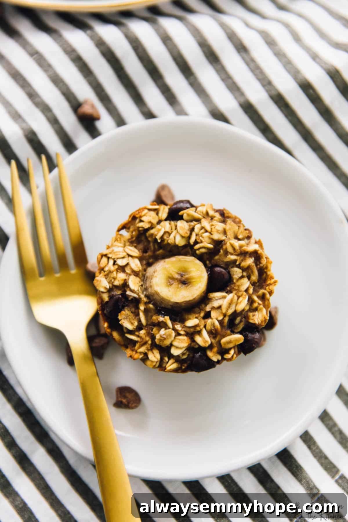 Top down shot of a single baked banana bread oatmeal cup on a plate with a gold fork on the side, ready to be enjoyed.