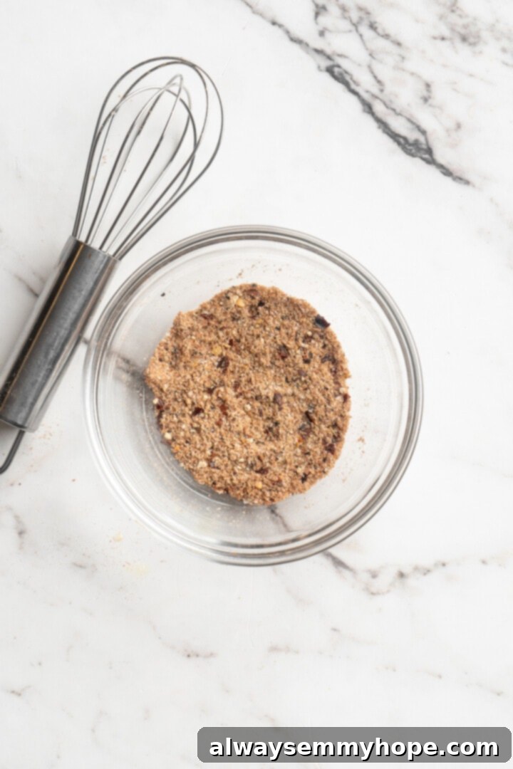 Overhead view of a small bowl filled with the vibrant homemade burrito bowl seasoning blend: garlic powder, paprika, cumin, salt, pepper, and red pepper flakes.