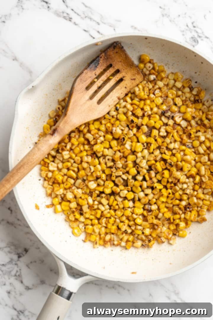 Overhead view of canned corn kernels charring in a hot skillet, showing the distinct blackened marks from high heat.
