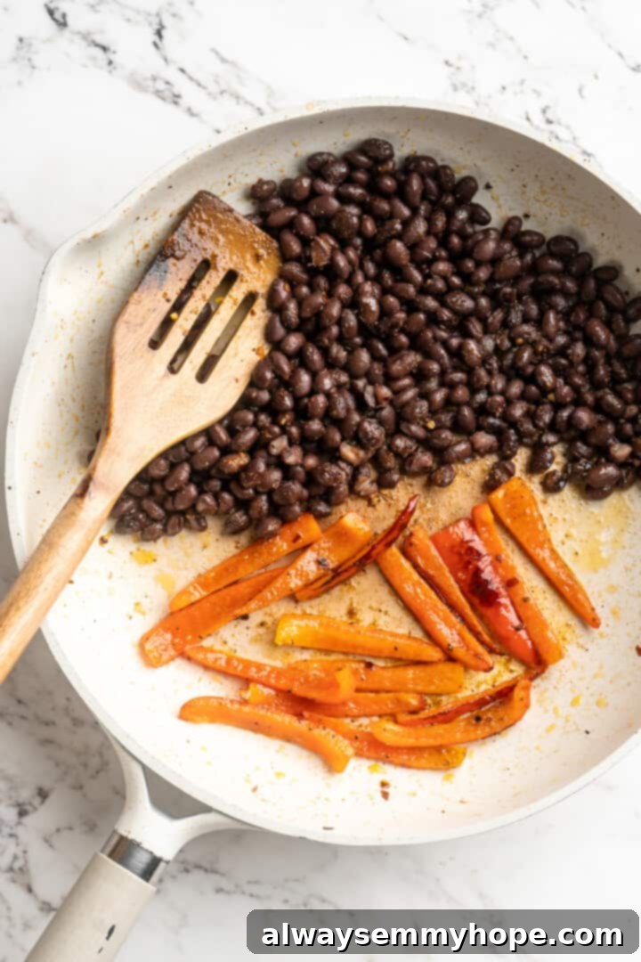 Overhead view of black beans and sliced red bell peppers cooking side-by-side in a skillet, seasoned with spices.