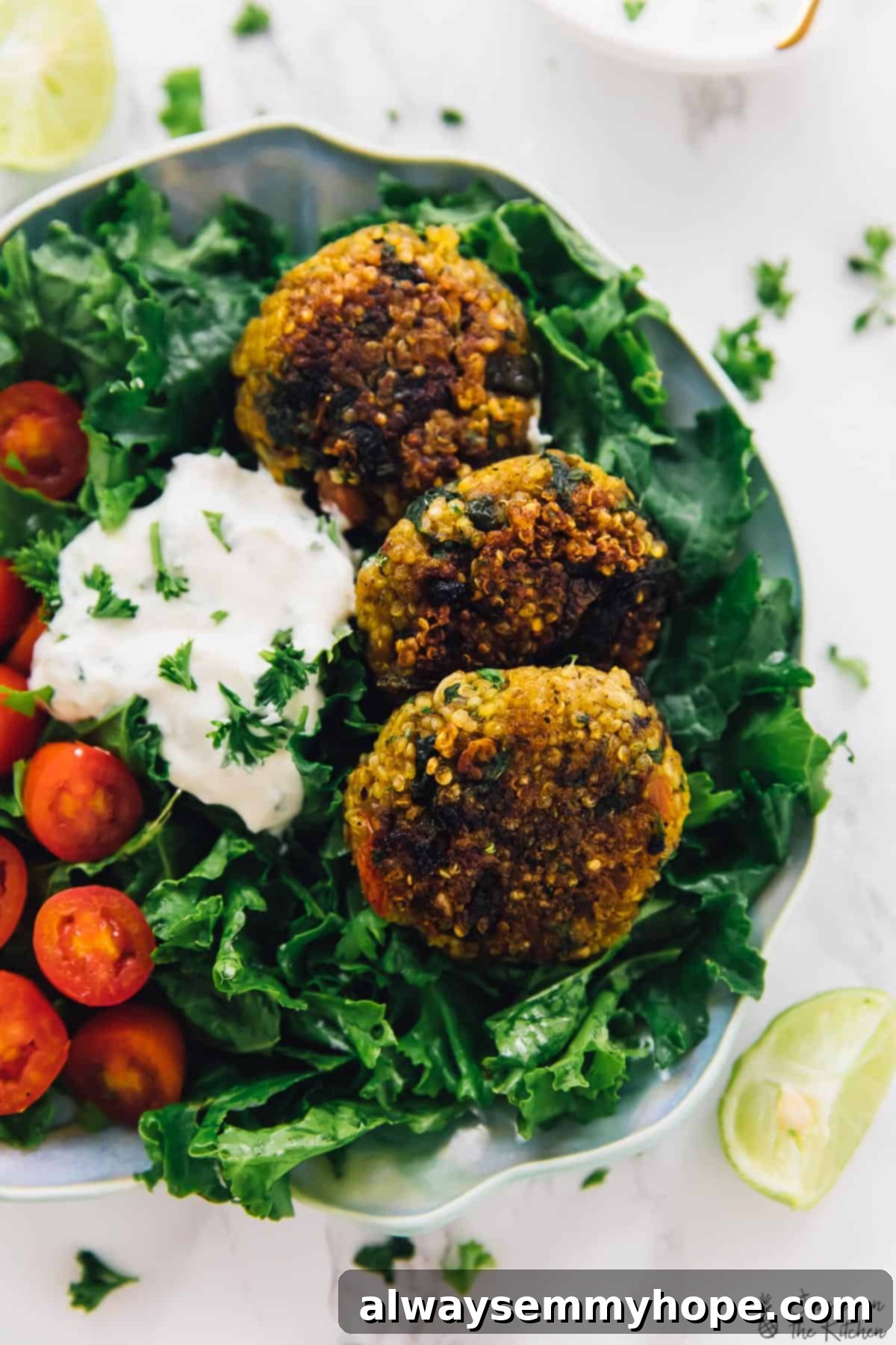 Three crispy quinoa patties on plate of greens with tomatoes and vegan yogurt sauce Three golden brown, crispy vegan quinoa patties arranged on a bed of fresh mixed greens with cherry tomatoes, drizzled with a creamy, light-colored tahini yogurt sauce.
