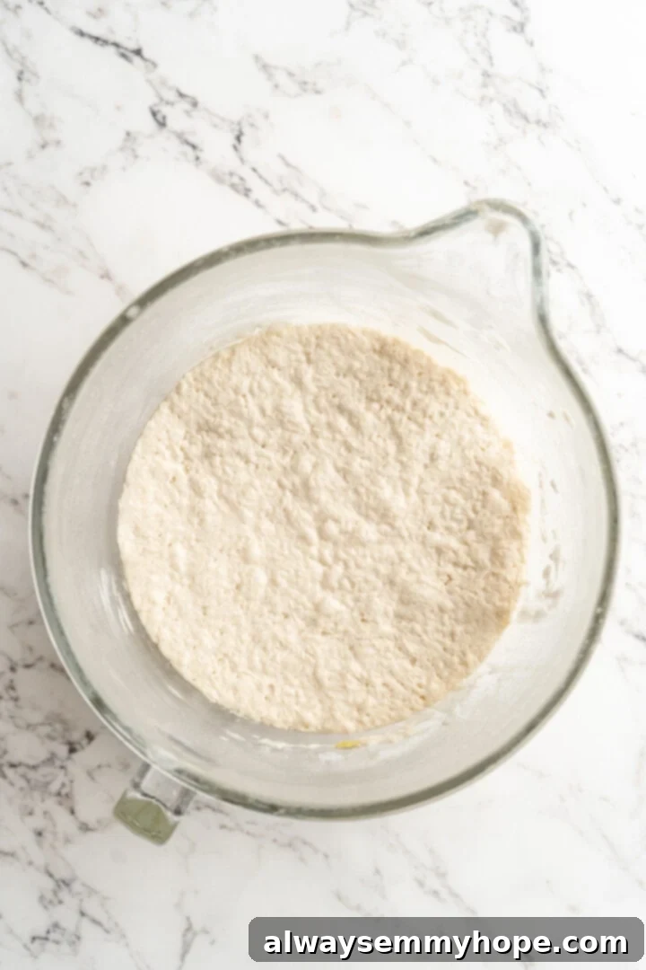 Gluten-free focaccia dough in a glass bowl after rising, visibly expanded and fluffy.