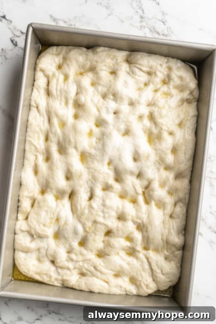 Gluten-free focaccia dough spread evenly on a baking sheet, ready for toppings.
