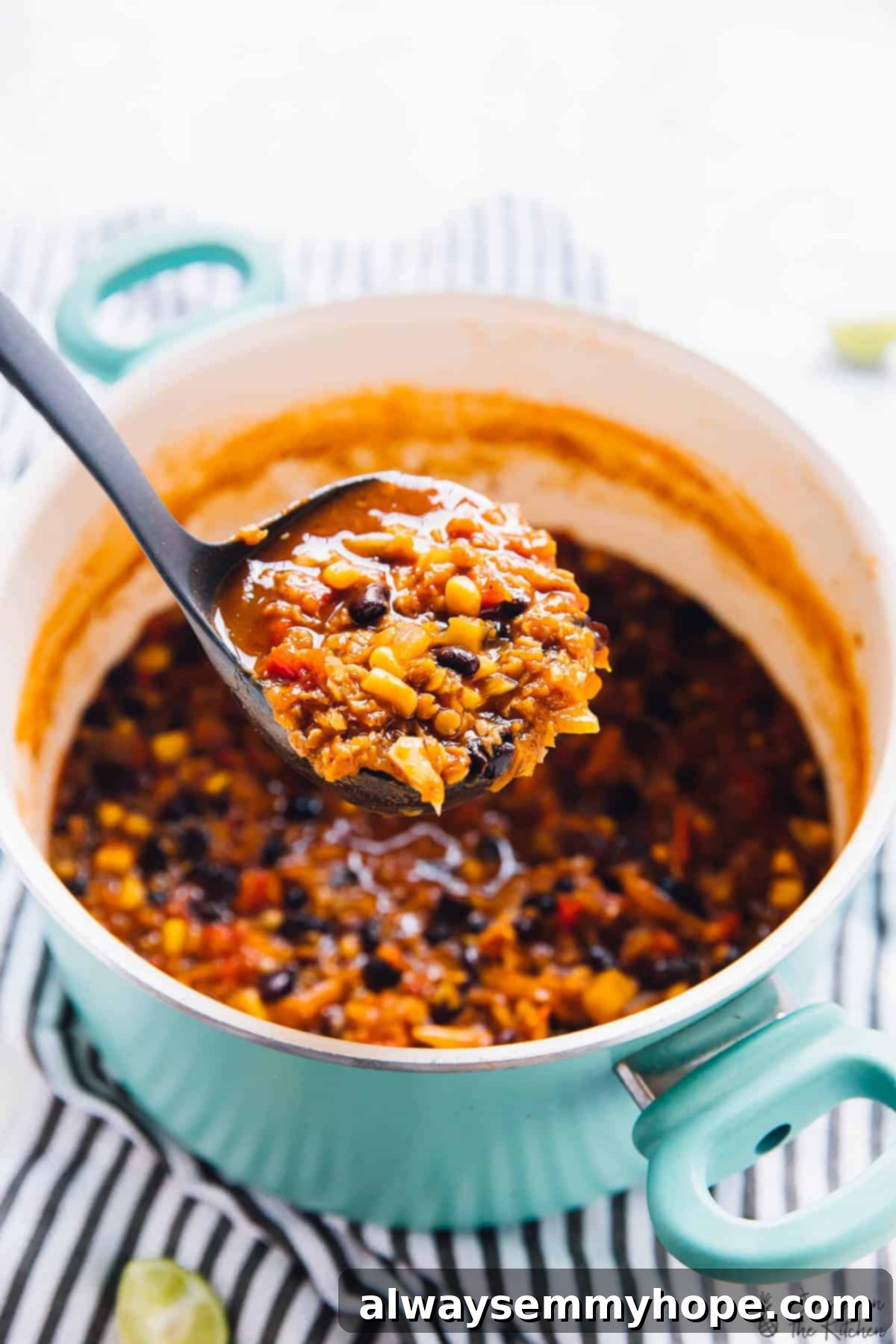 A ladle expertly scoops a serving of rich red lentil chili from a blue pot, showcasing its thick consistency and inviting texture, ready to be enjoyed.